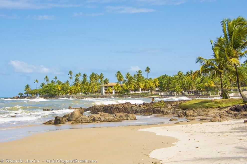 Imagem de uma moça admirando as pedras e o mar da Praia Back Door-Ilhéus.